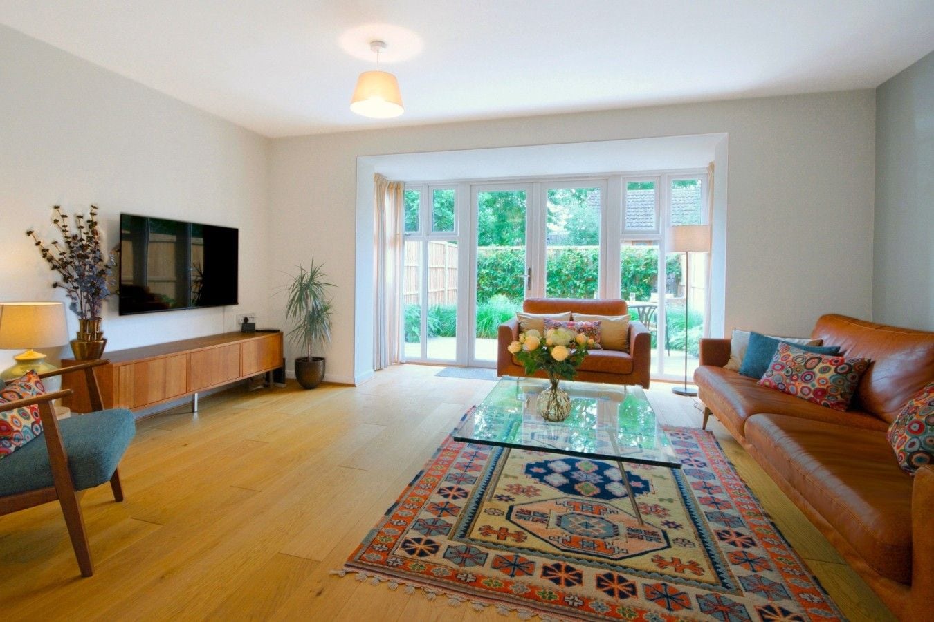 Ein geräumiges Wohnzimmer mit einem großen Fenster, einem Flachbildfernseher, einer Couch, einem Couchtisch und einem gemusterten Teppich.