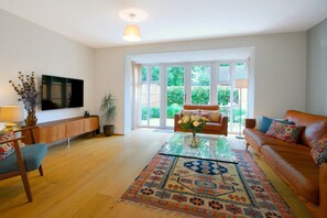 A spacious living room with a large window, a flat-screen TV, a sofa, a coffee table, and a patterned rug. - Modern Spacious Two bed house close to Cambridge (Cottenham)