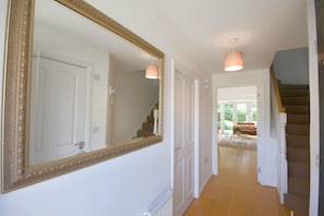 A hallway with a large mirror, a staircase, and a view into a living area with a couch and a coffee table. - Modern Spacious Two bed house close to Cambridge (Cottenham)