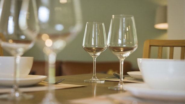 Uma mesa de jantar com duas taças de vinho e uma tigela, posta para uma refeição.