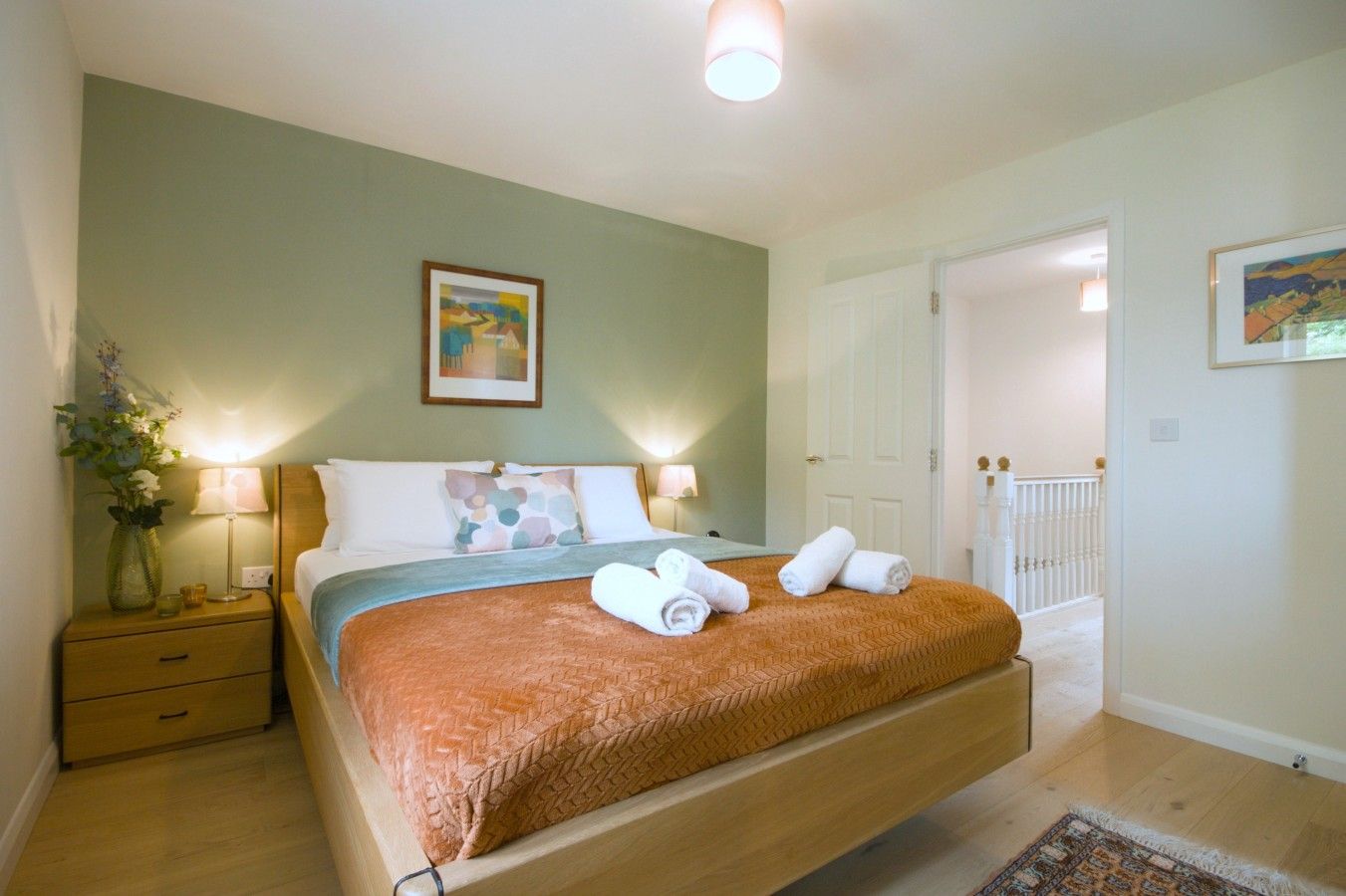 Une chambre d’hôtel avec un lit, des lampes de chevet, une table de nuit, un vase avec des fleurs et un tableau au mur.
