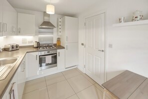 A modern kitchen with stainless steel appliances, white cabinetry, and a wooden dining table.