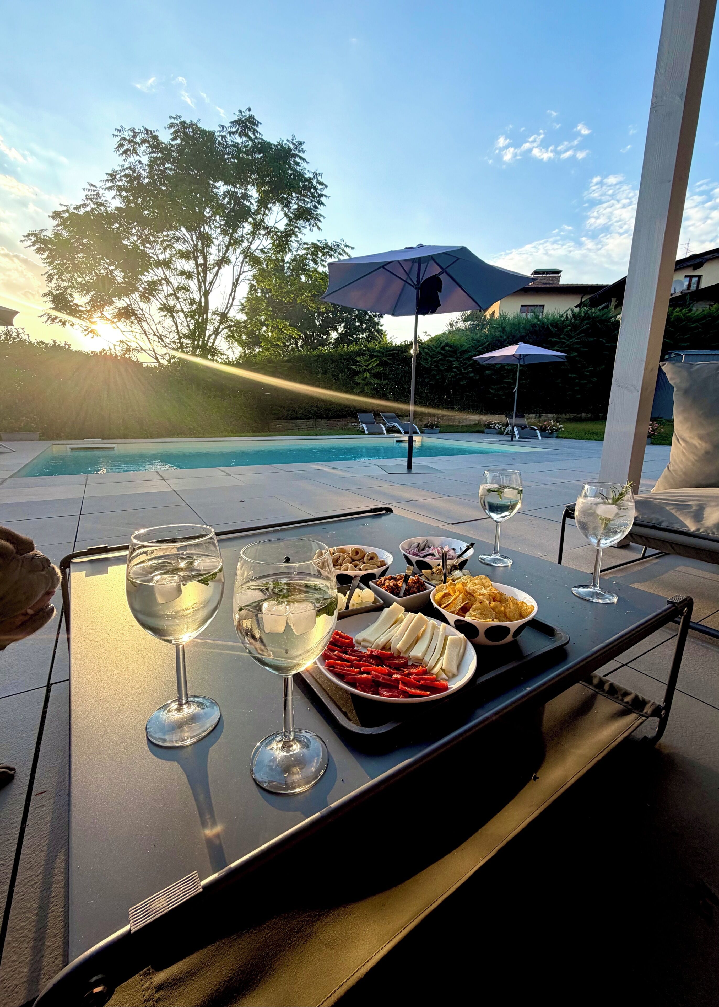 Un'area pranzo a bordo piscina con un tavolo, bicchieri da vino e diversi snack.