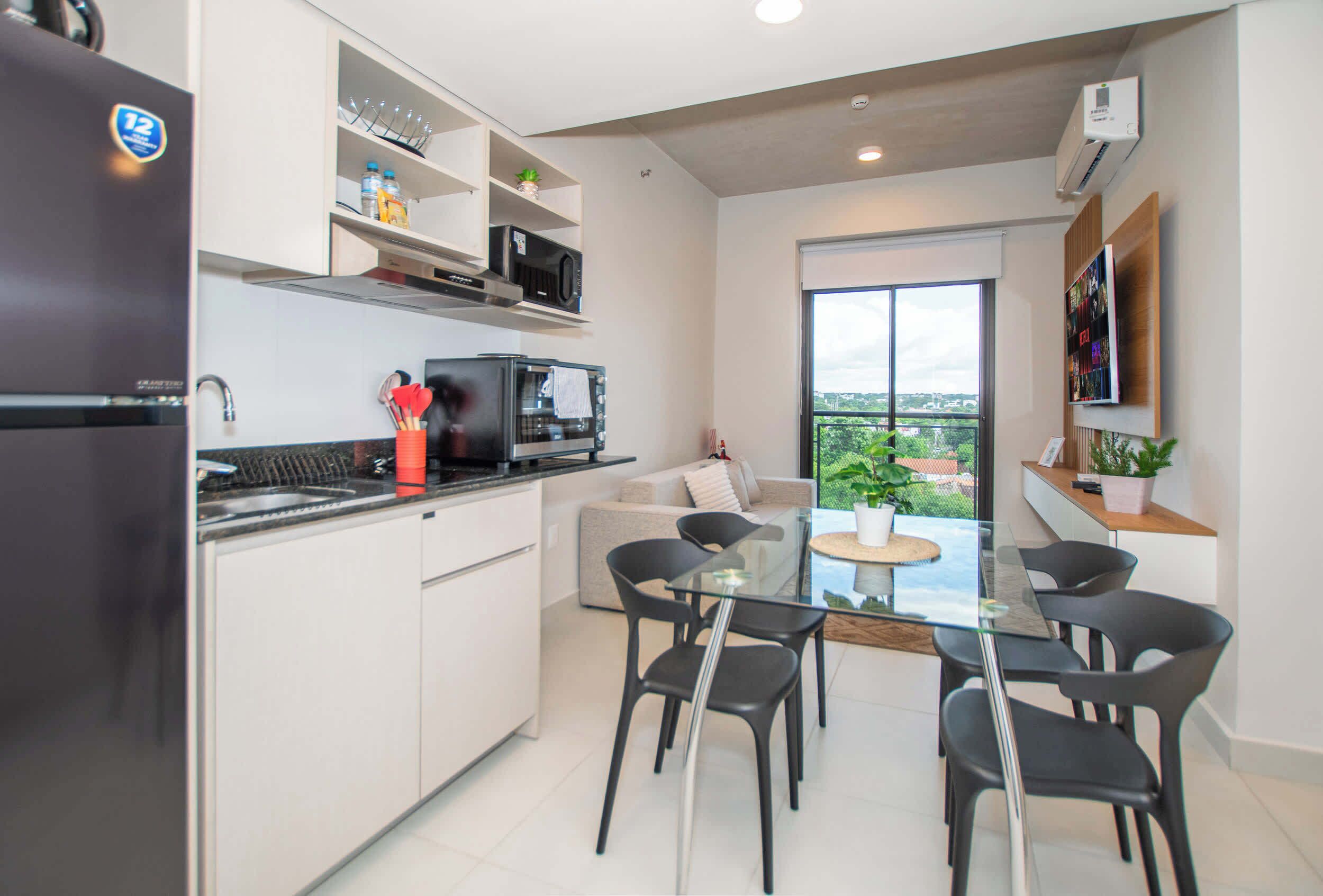 Een moderne keuken met een koelkast, magnetron en fornuis, een eethoek met een glazen tafel en stoelen, en een balkon met uitzicht.
