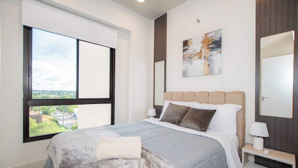 Una camera da letto moderna con un'ampia finestra, un letto con copripiumino grigio e bianco, una testiera in legno e un comodino con una lampada.