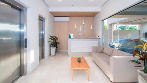 Una moderna area reception con un divano, una scrivania in legno, un tavolino da caffè e un'auto visibile dalla finestra.