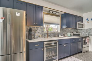 A modern kitchen with stainless steel appliances, dark blue cabinets, a built-in microwave, and a window with a view. - Walk to Beach & Dining! Unique St. Pete Getaway (St Pete Beach)
