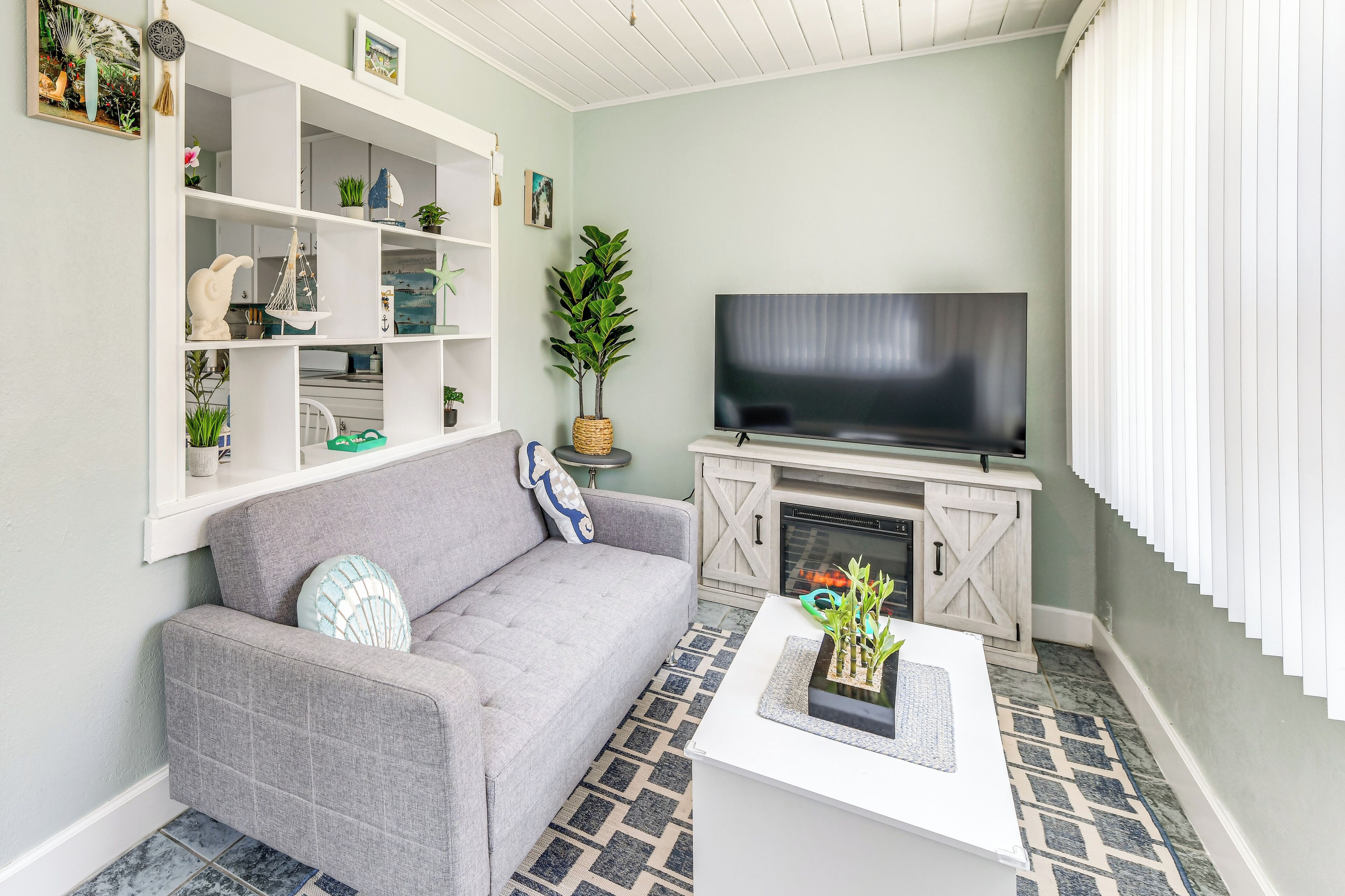 A living room with a grey sofa, a flat-screen TV, a white fireplace, and a patterned rug.