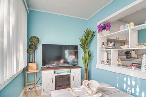 A living room with a flat-screen TV, a fireplace, a white sofa, and a shelving unit with decorative items. - Walk to Beach & Dining! Unique St. Pete Getaway (St Pete Beach)