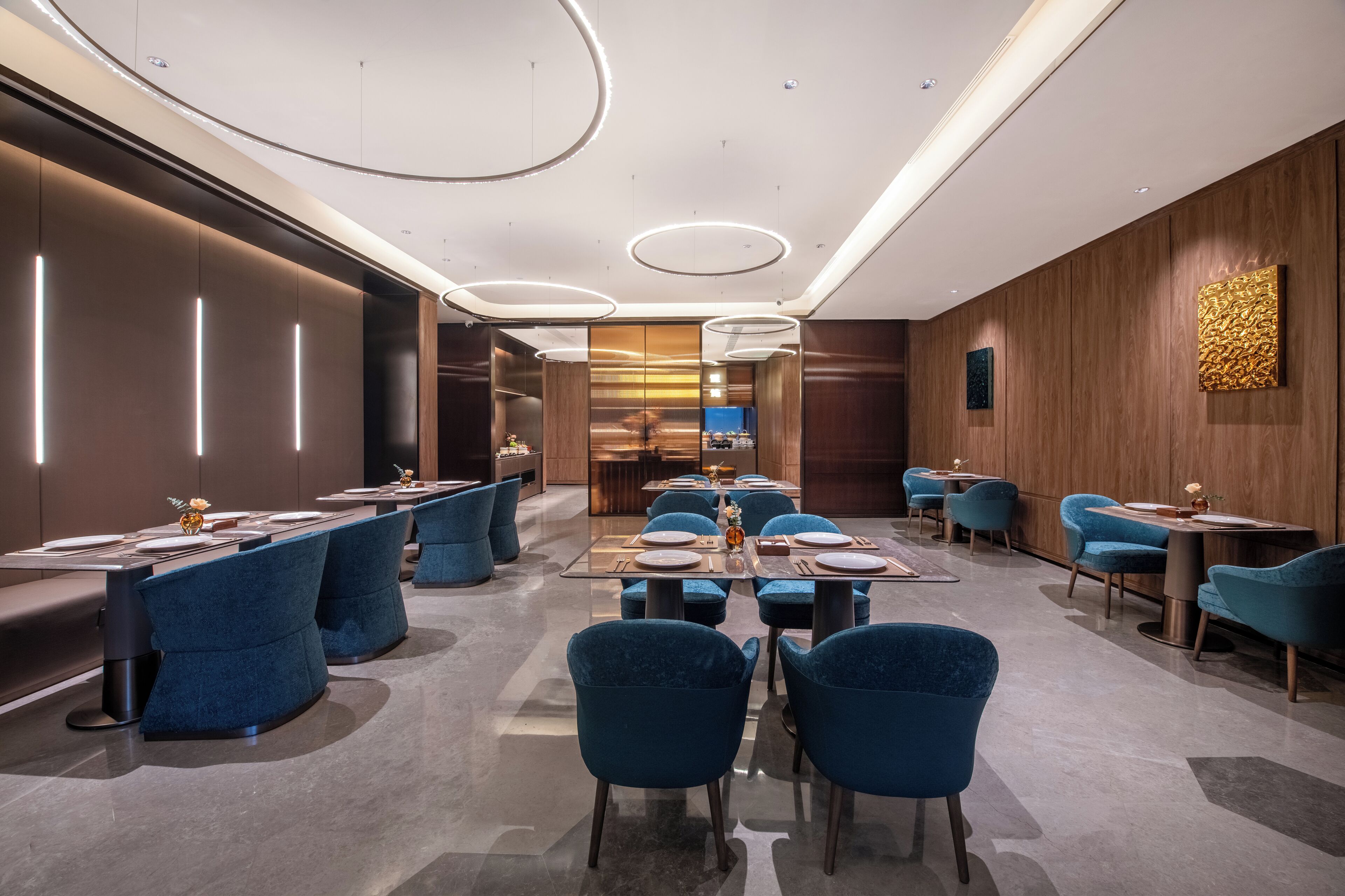 Un comedor moderno con mesas redondas, sillas tapizadas en azul y una zona de bar central.