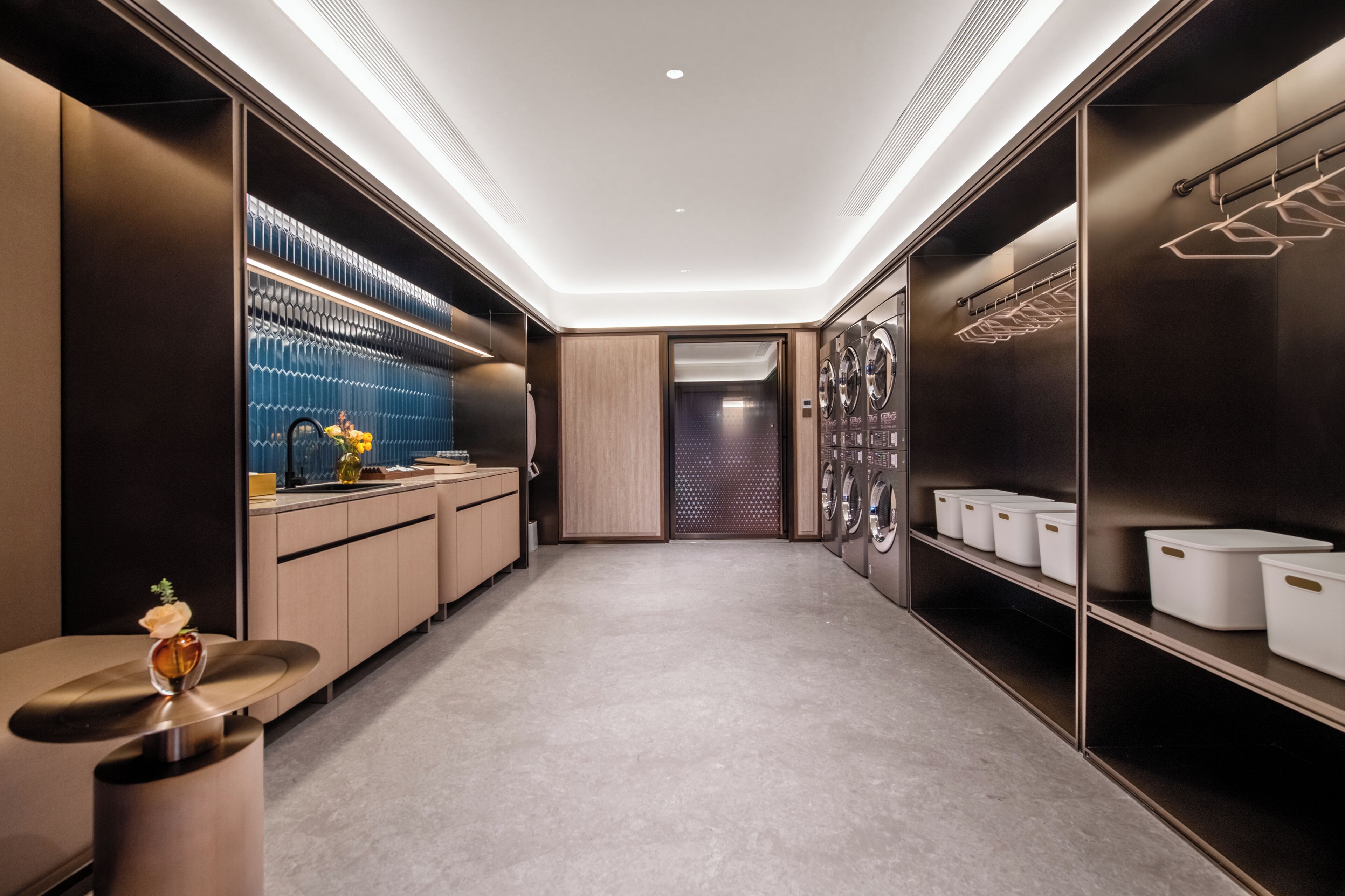 Une buanderie moderne dans un hôtel, équipée d’une machine à laver centrale, d’un étendoir et de bacs de rangement bien organisés.