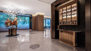 A modern lobby with a reflective floor, a chandelier, a display cabinet, and a large window with a forest view. - Crystal Hotel Hangzhou Xixigu Tianmushan (Hangzhou)