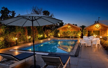 A swimming pool with lounge chairs and an umbrella, surrounded by wooden buildings and greenery.