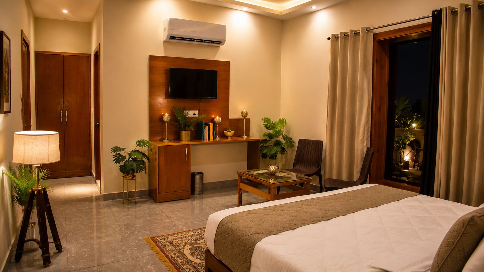 A hotel room with a bed, a desk with a TV, a chair, a small table, and a window with curtains.