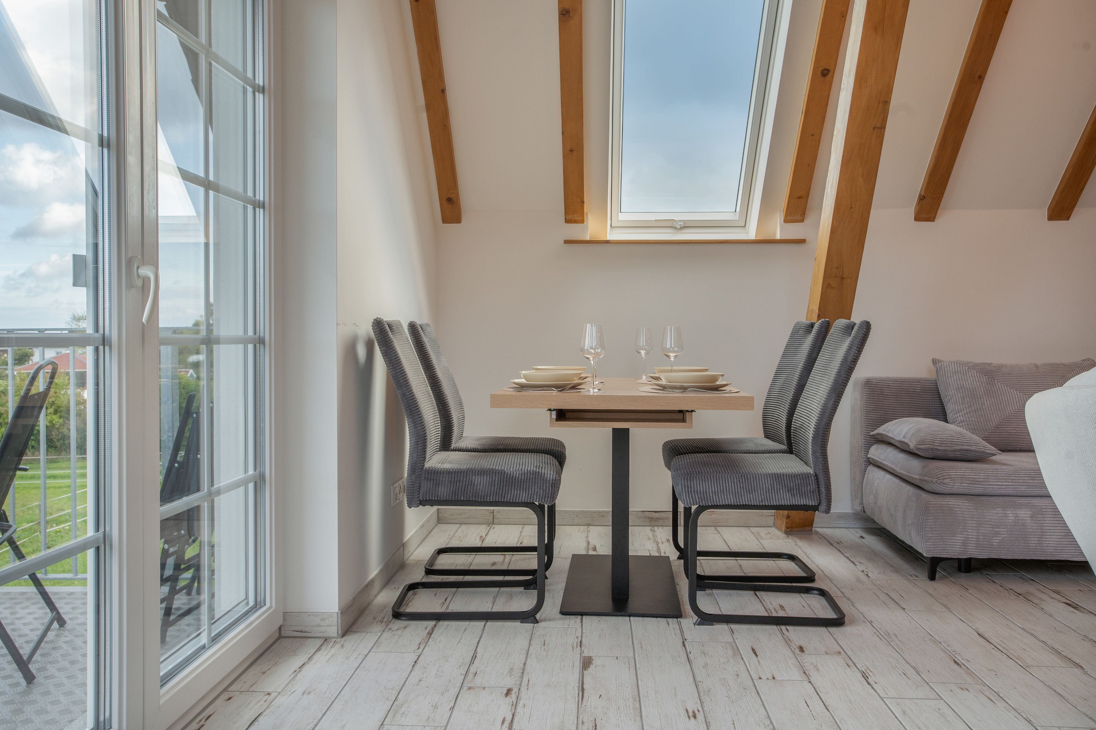 Un área de comedor con una mesa, sillas, un sofá y ventanas amplias con vistas.