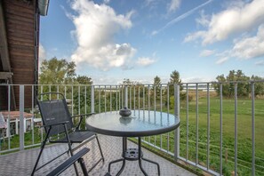 Ein Balkon mit einem runden Glastisch und zwei Stühlen mit Blick auf eine Wiese.