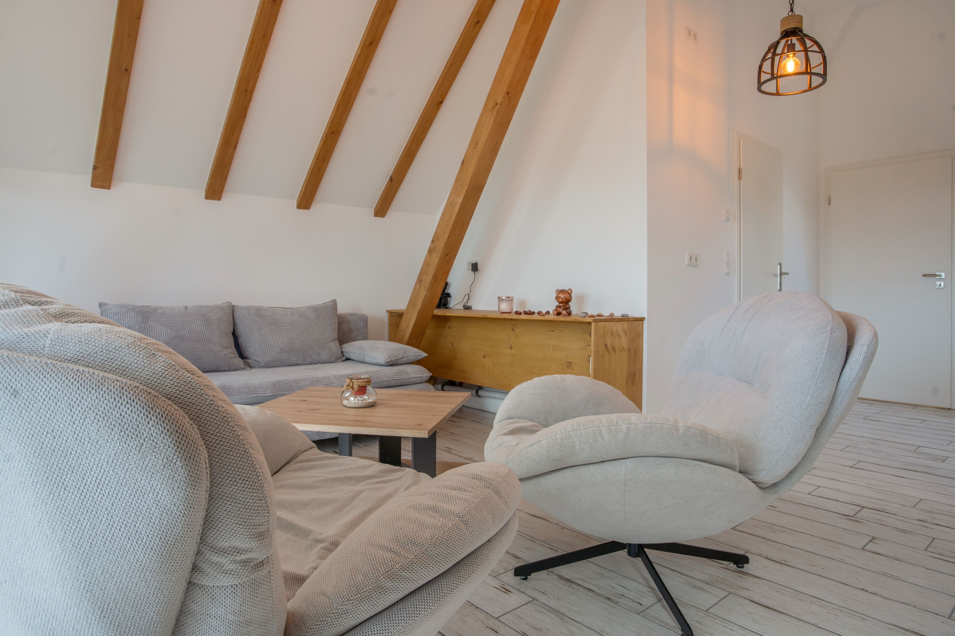 A cozy loft-style room with a sloped ceiling, a wooden bench, a cushioned armchair, and a small table with a candle.
