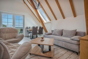 A loft-style room with a sloped ceiling, a sofa, a chair, a small table, and a view through a large window.