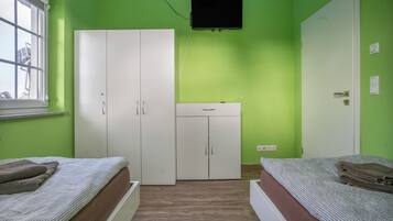 Ein Zimmer mit zwei Betten, einem Kleiderschrank, einem an der Wand montierten Fernseher und einem Fenster.