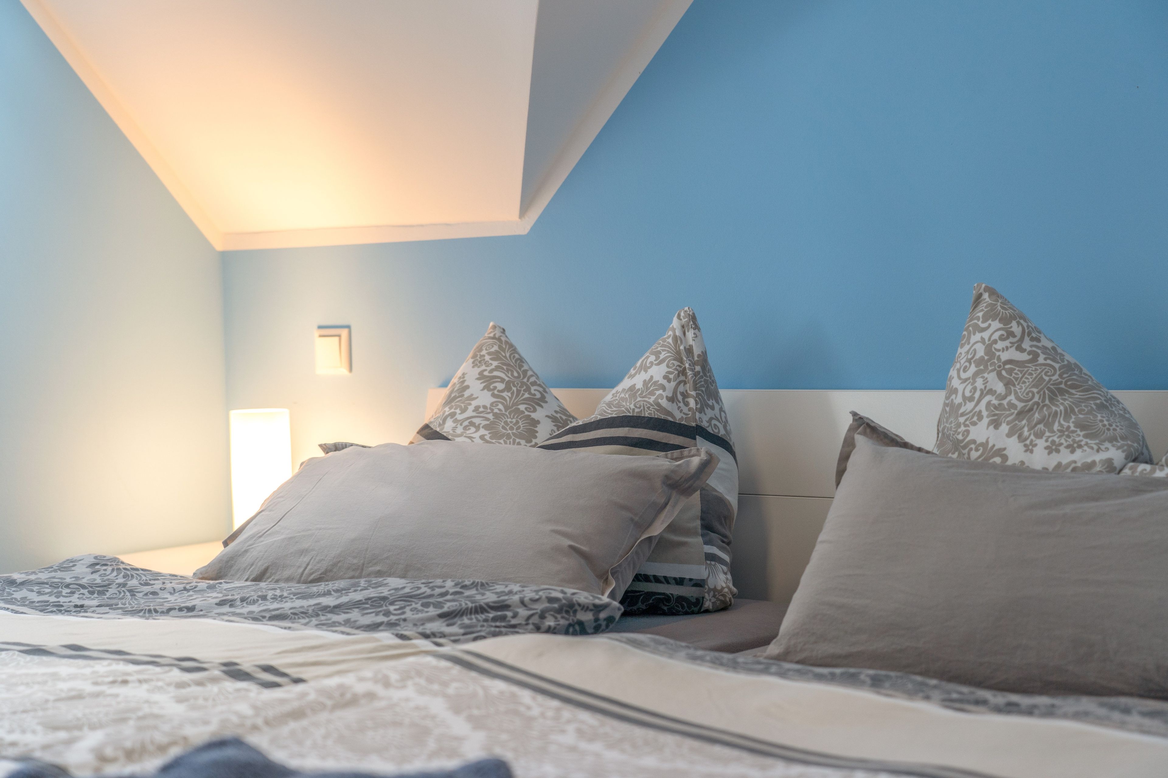 Un dormitorio con cama, almohadas, una mesita de noche y una lámpara de pared.
