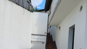 Ein schmaler Innenhof mit Backsteinpflasterung, einer weißen Mauer mit Briefkästen und einem Holzzaun.