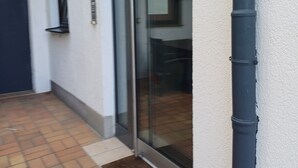 Ein Gebäudeeingang mit Glastür, kleinem Fenster und Fliesenboden.