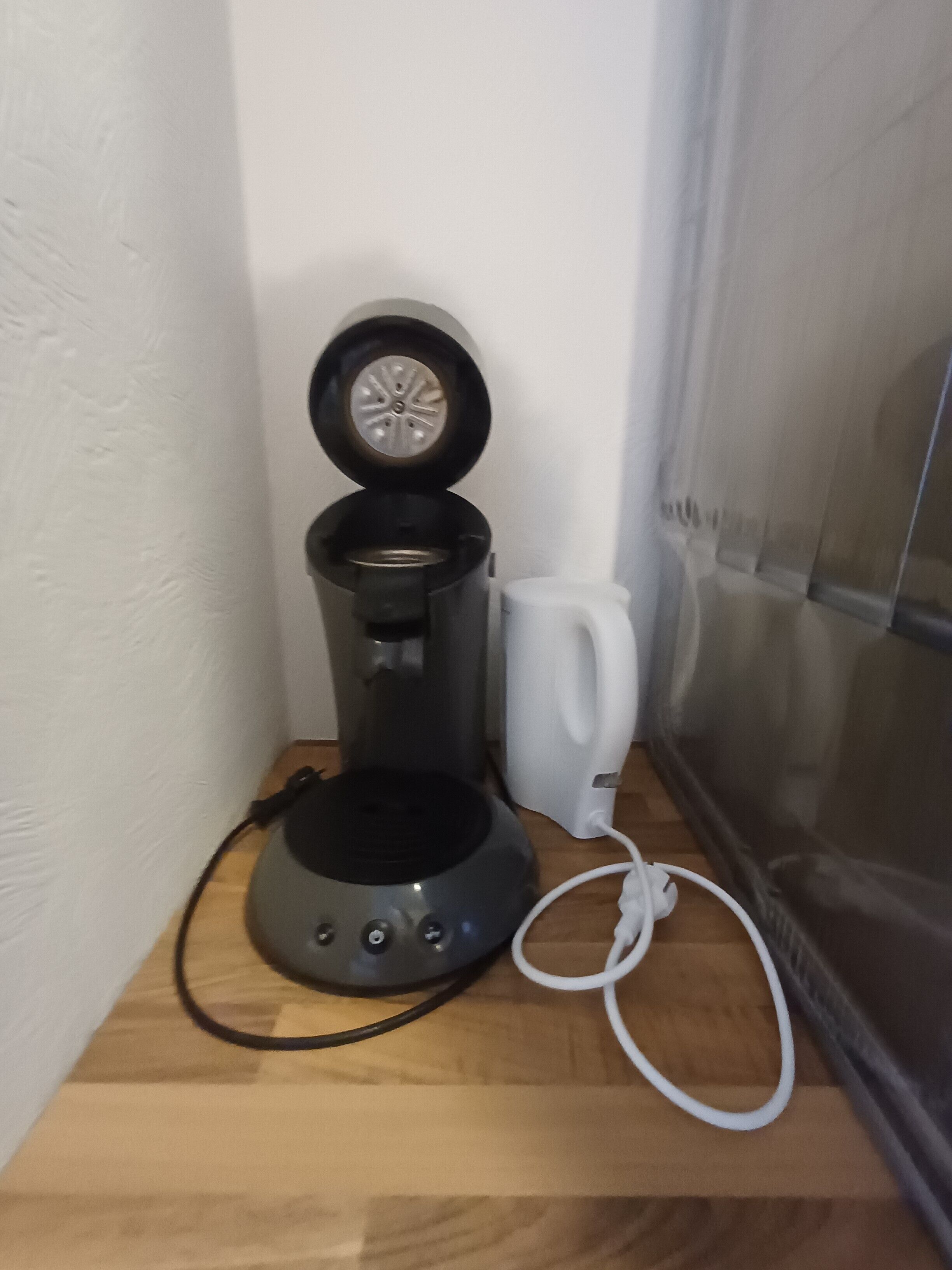 Een koffiezetapparaat op een houten oppervlak, met een witte mok ernaast.
