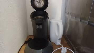 Een koffiezetapparaat op een houten oppervlak, met een witte mok ernaast.