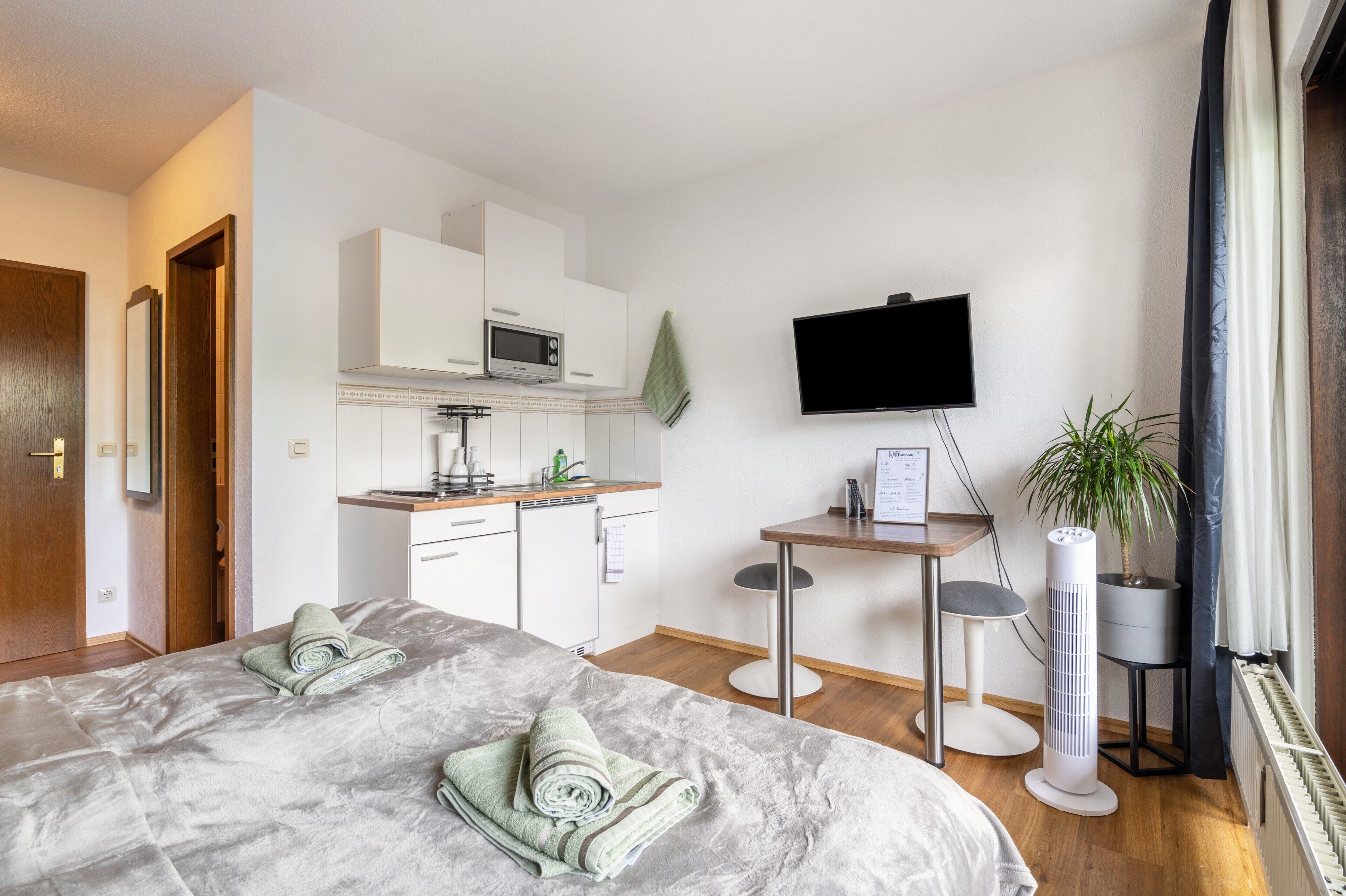 Ein modernes Hotelzimmer mit einem Bett, einer Küchenzeile, einem Flachbildfernseher und einer Topfpflanze.