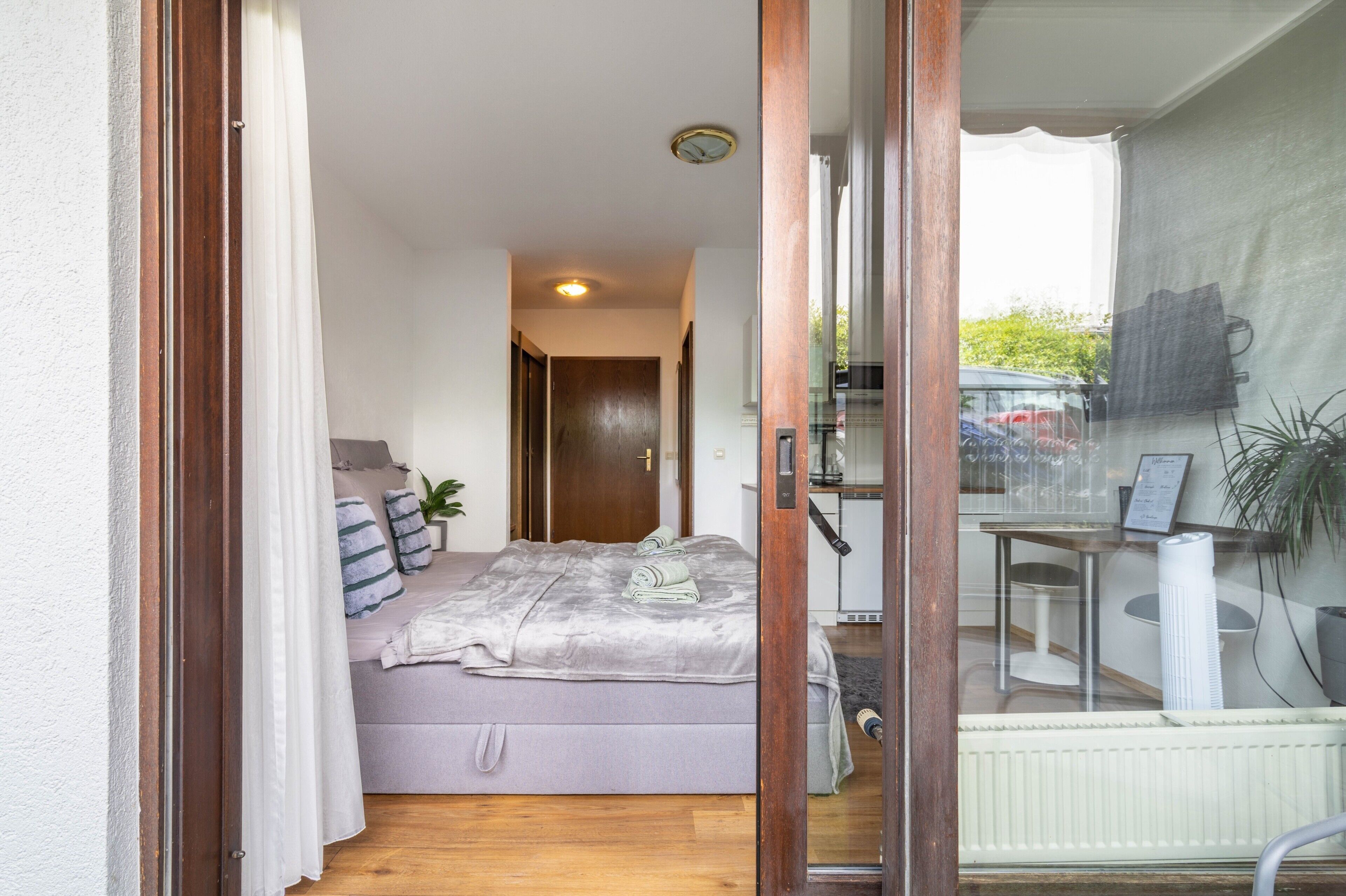 Un dormitorio con cama, almohadas, mesita de noche, ventana y vistas al exterior.