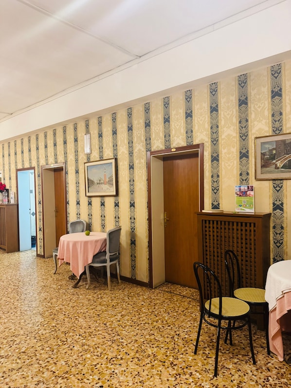 Habitació d'hotel amb paper pintat estampat, terra de rajola, una taula de menjador amb estovell rosa i una cadira.