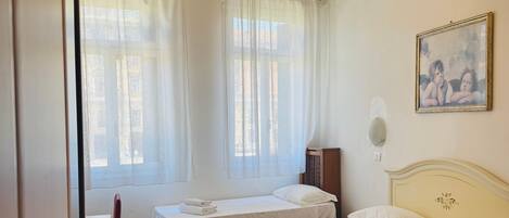 A hotel room with two beds, a chandelier, a painting, and a window with curtains.