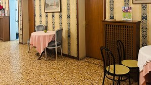 A hotel room with a patterned wallpaper, a tiled floor, a dining table with a pink tablecloth, and a chair. - Double Room 3 with Wi-Fi and Air Conditioning (Venice)