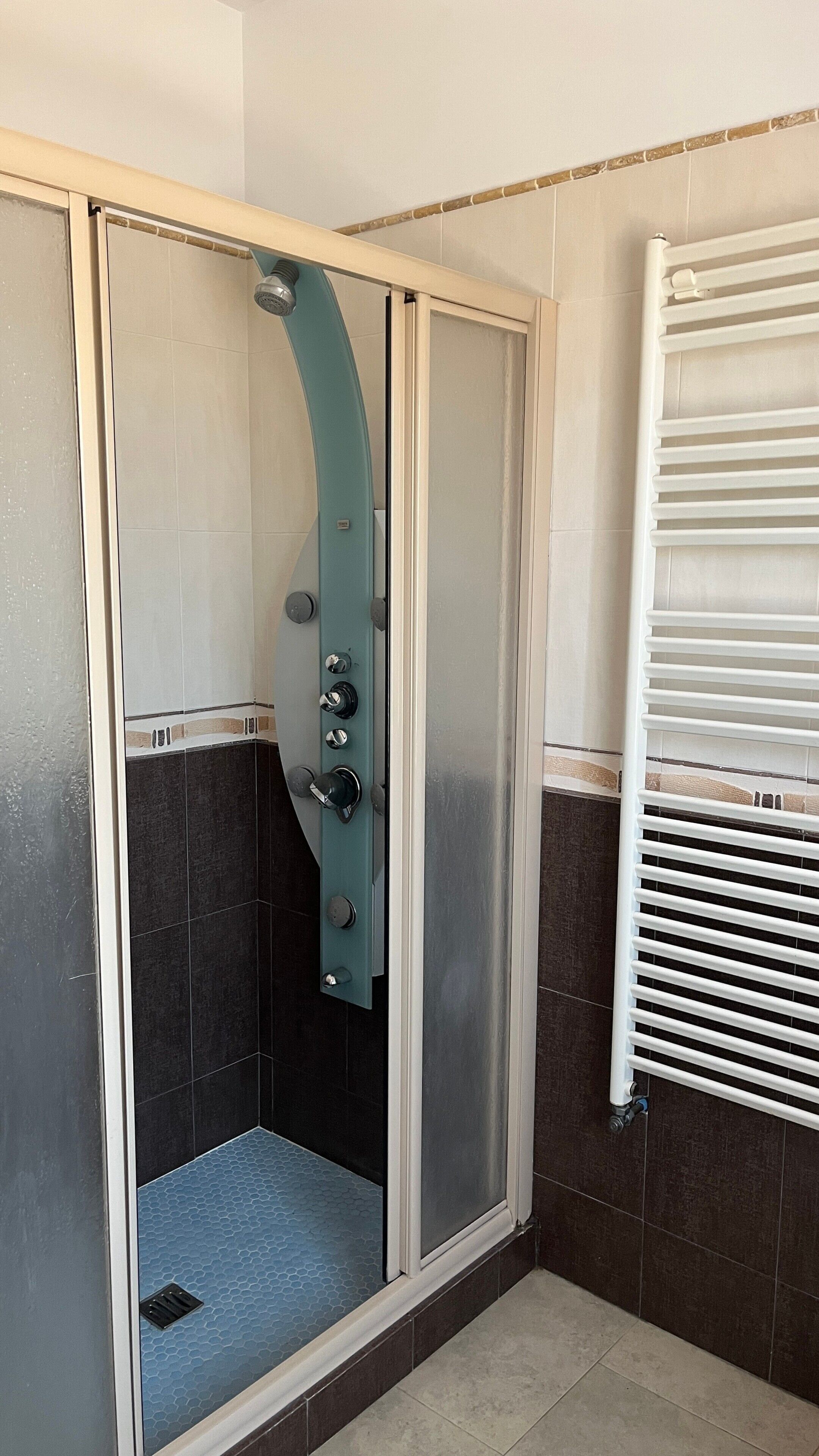 A shower enclosure with a frosted glass door, a control panel with multiple knobs, and a white radiator on the wall.