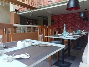 Ein Restaurant mit Holztischen und -stühlen, einer Wand mit Muster und hängenden Pendelleuchten.