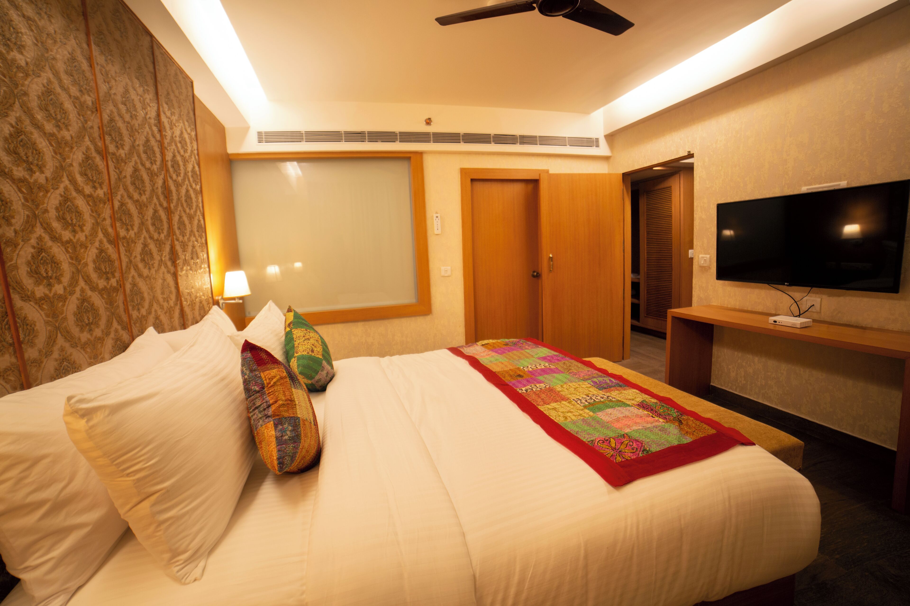 A hotel room with a bed, a television, a ceiling fan, and a wardrobe.
