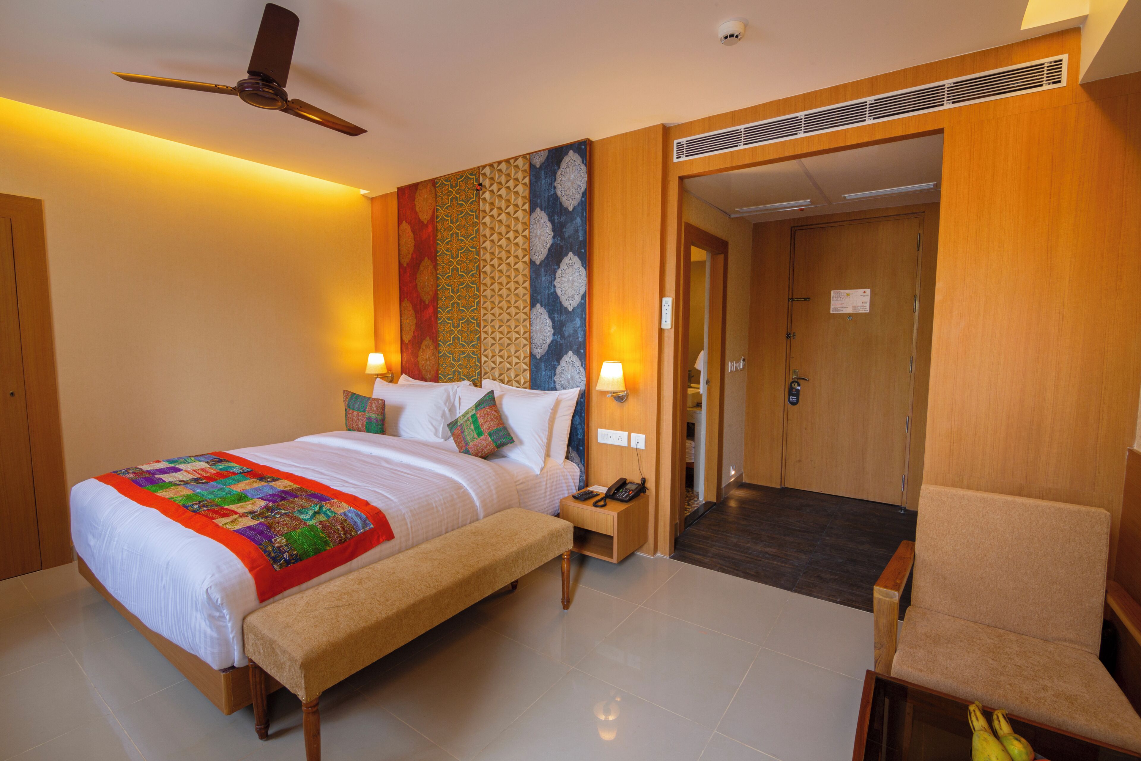 A hotel room with a bed, bedside tables, a chair, a desk, a phone, and a ceiling fan.