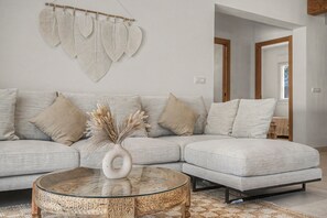 A modern living room with a sectional sofa, a glass coffee table, and a wall-mounted decorative piece. - Villa Pinar in Conil with Private Pool, Wi-Fi, and Air Conditioning (Conil de la Frontera)