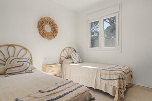 Une chambre avec deux lits simples, une table de chevet, un élément de décoration circulaire fixé au mur et une fenêtre donnant sur des arbres.