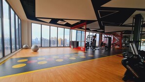 Ein Fitnessstudio mit großen Fenstern, Trainingsgeräten und einem Holzboden mit farbigen Markierungen.