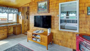 L’intérieur d’un chalet en bois est aménagé avec un téléviseur, des meubles en bois, une cheminée et une fenêtre donnant sur un paysage pittoresque.