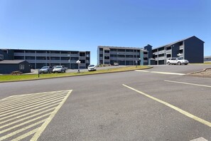 A parking lot with cars, a building with multiple floors, and a clear sky.