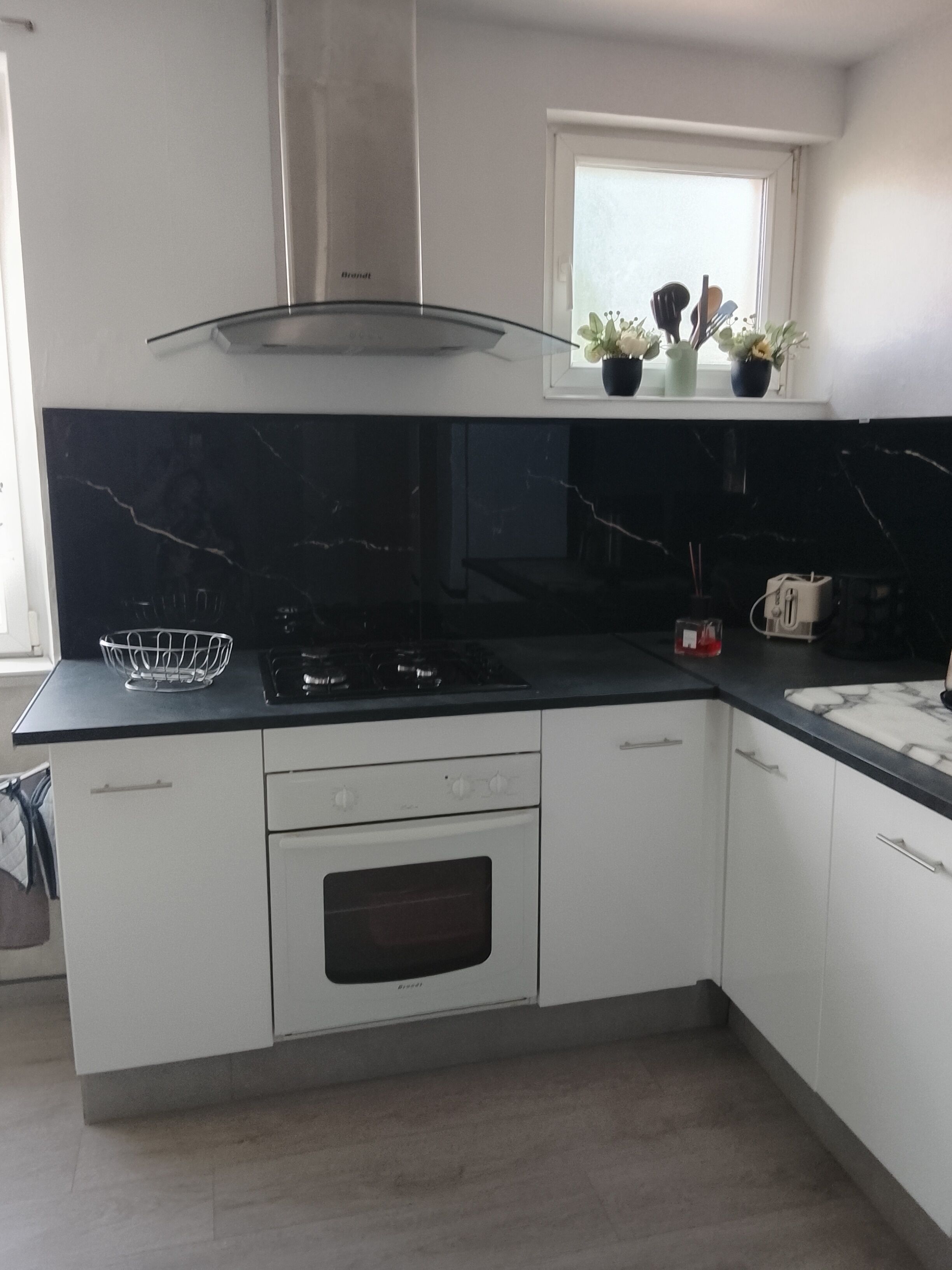 A modern kitchen with white cabinets, a black countertop, a stainless steel range hood, and a window with potted plants.