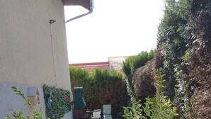 A patio with a table and chairs, potted plants, and a wall-mounted grill.