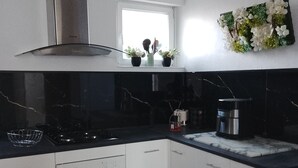 A modern kitchen with white cabinets, a black countertop, a stainless steel range hood, and a window with potted plants.