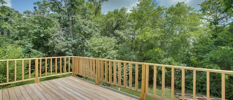 Una terraza de madera con barandilla, rodeada de abundante follaje verde y árboles.