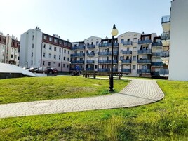 A residential building with multiple balconies, a paved pathway, and a grassy area.