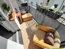 A balcony with wicker furniture, potted plants, and a mesh safety barrier.