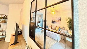 Un intérieur moderne avec un grand miroir qui reflète un salon, un téléviseur à écran plat et un coin cuisine.
