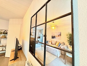 A modern interior with a large mirror reflecting a living room, a flat-screen TV, and a kitchen area. - Charming House in Tournefeuille_ Parking (Tournefeuille)